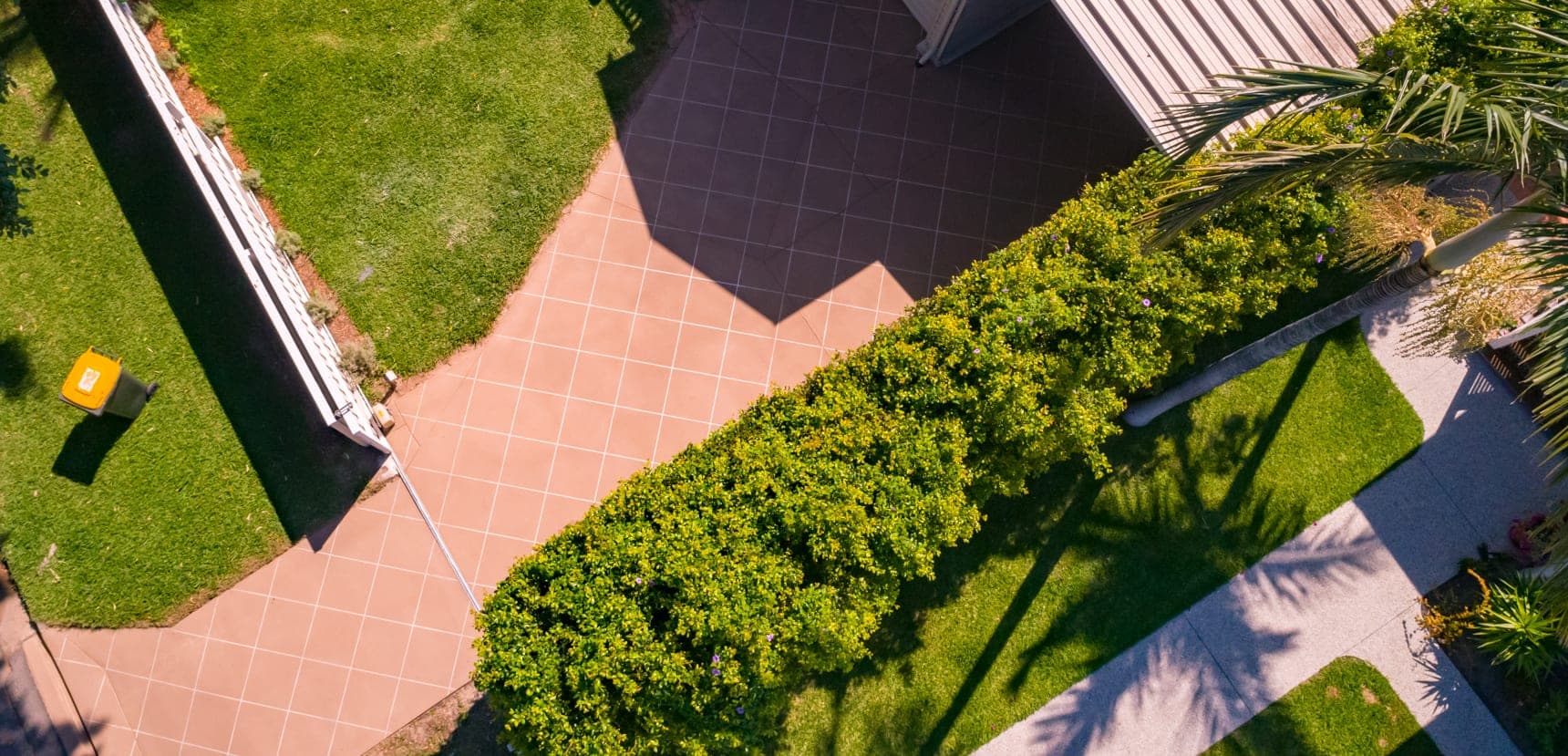 Beige Covercrete driveway with white angled-square Stencil lines, running from the front of the block past a hedge to the house.