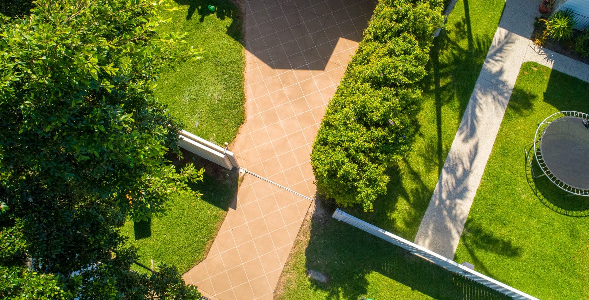 Drone view of a long Beige Covercrete driveway with a white angled-square Stencil, running between a lawn and a tall hedge.