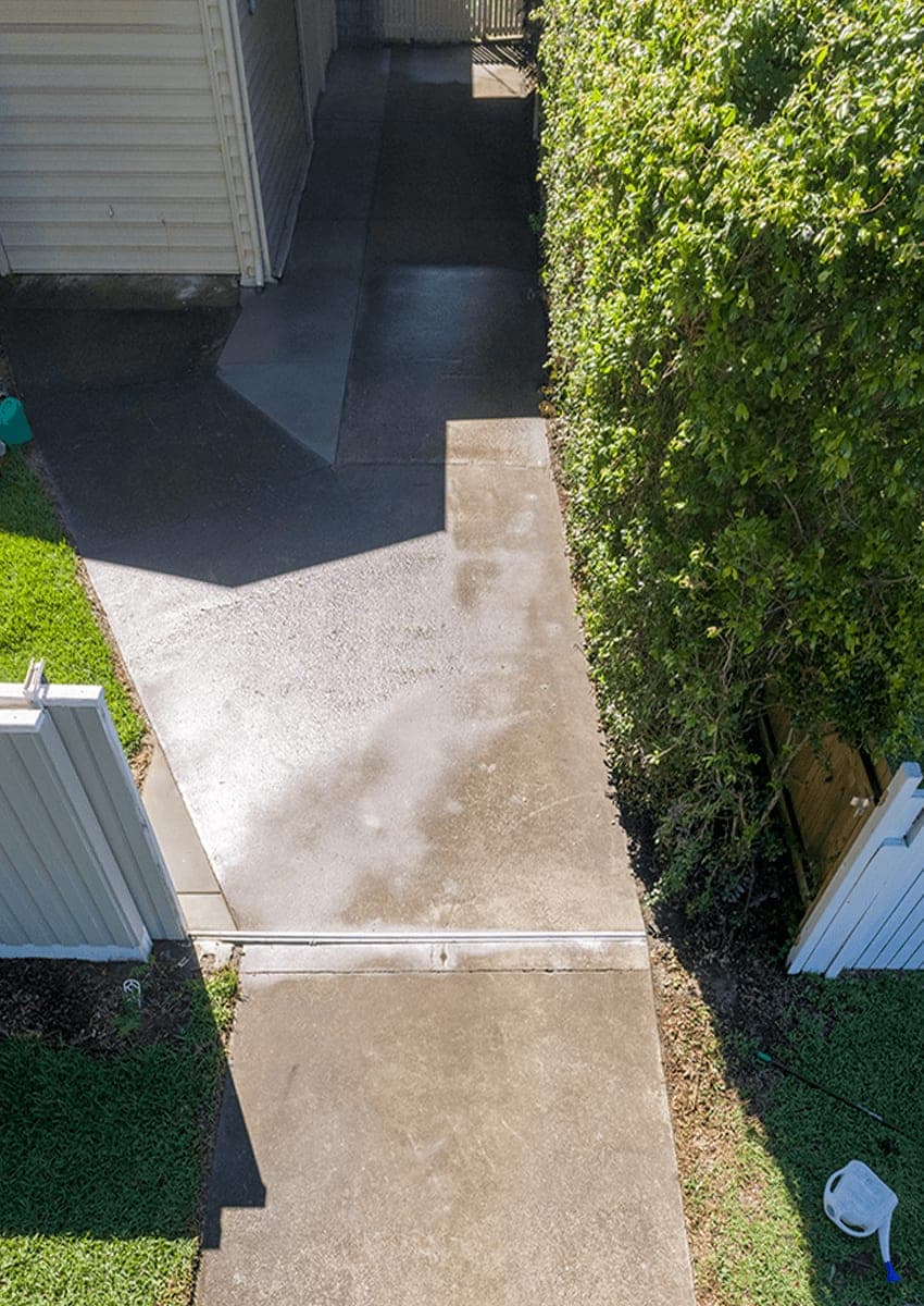 Before: a plain grey concrete side path, stained and patchy, running between a fence and a hedge.