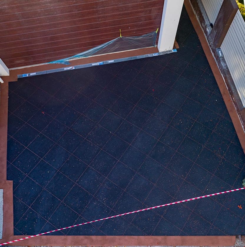 After: the same driveway covered in Black Sand Covercrete, with red angled-square Stencil lines and a red border.