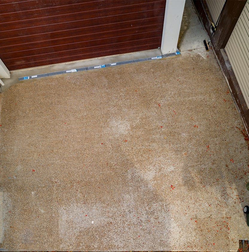 Before: the driveway as faded exposed aggregate concrete in front of the garage, scattered with fallen red petals.