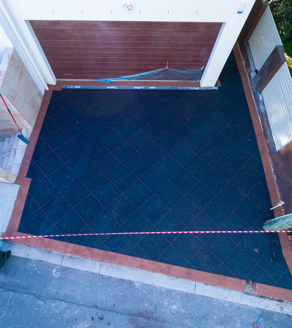 Looking down on a short driveway in Black Sand Covercrete with red angled-square Stencil lines and a red border, finished from the garage door to the footpath.