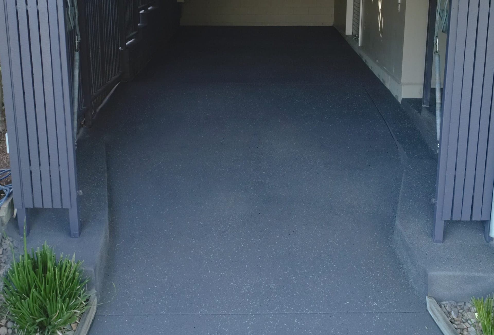 Dark grey Covercrete with light flecks running up a ramp between open slatted gates and into an under-house garage, with the raised edges either side finished to match.