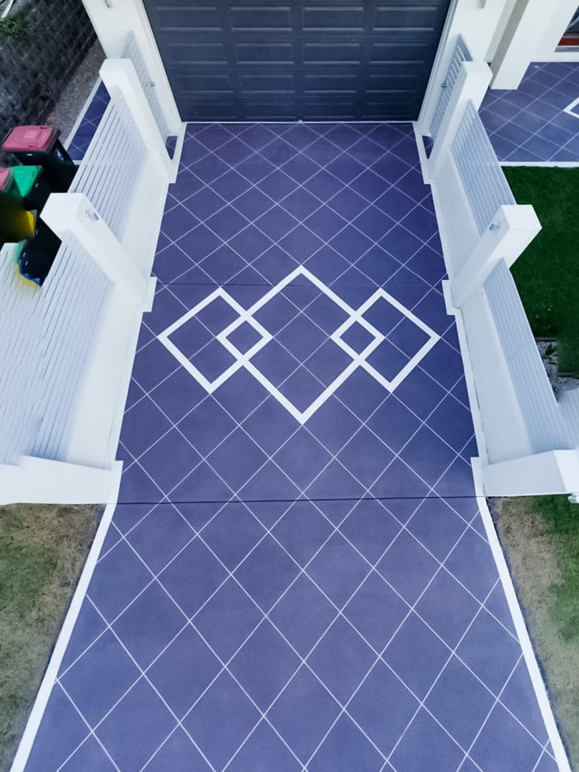 Looking straight down on a Purple Graphite Covercrete driveway between white fence posts, with fine white Stencil lines and overlapping diamond panels.