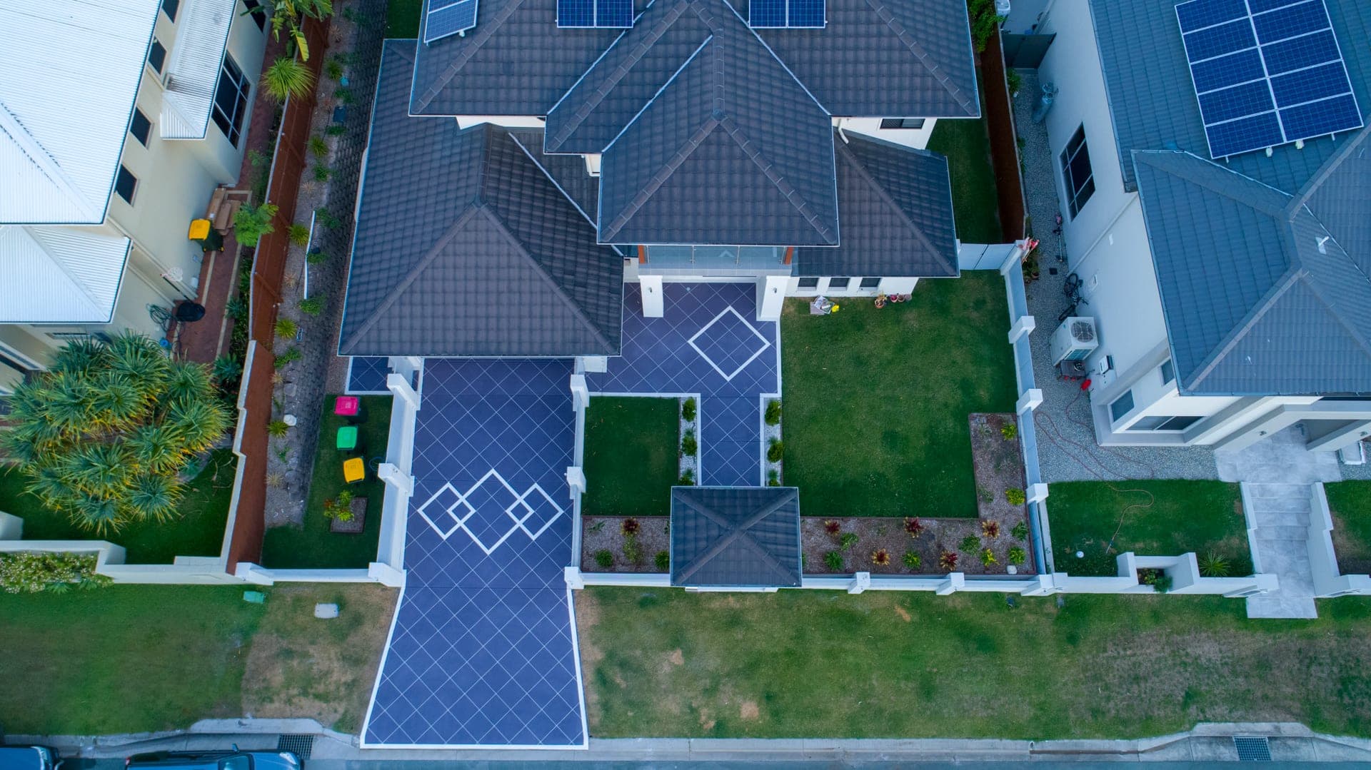 Drone view looking down on a two-storey home with a Purple Graphite Covercrete driveway, entry path and front porch, set out in an angled-square Stencil with white borders and diamond feature panels.